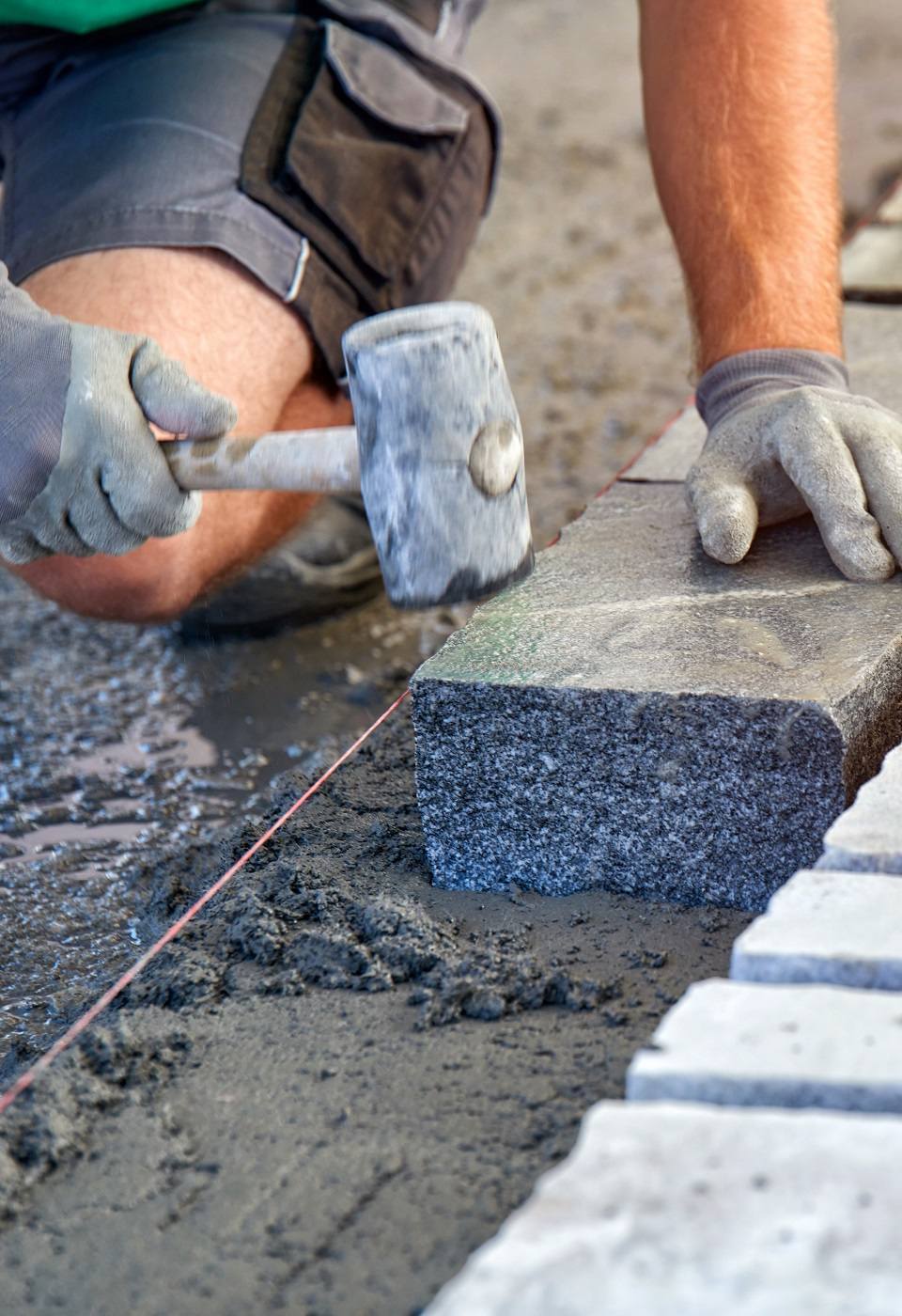 A workman's gloved hands use a hammer to place stone pavers. Wor