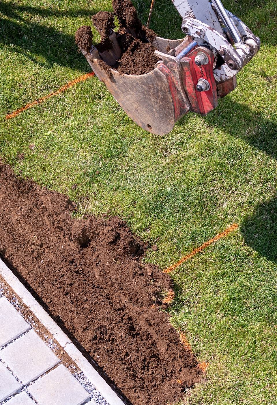 Bagger hebt ein Findament für einen Gartenzaun aus